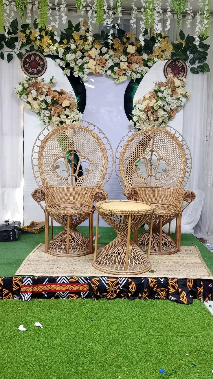 Deux fauteuils en rotin à haut dossier rond et une petite table, devant un décor de fleurs