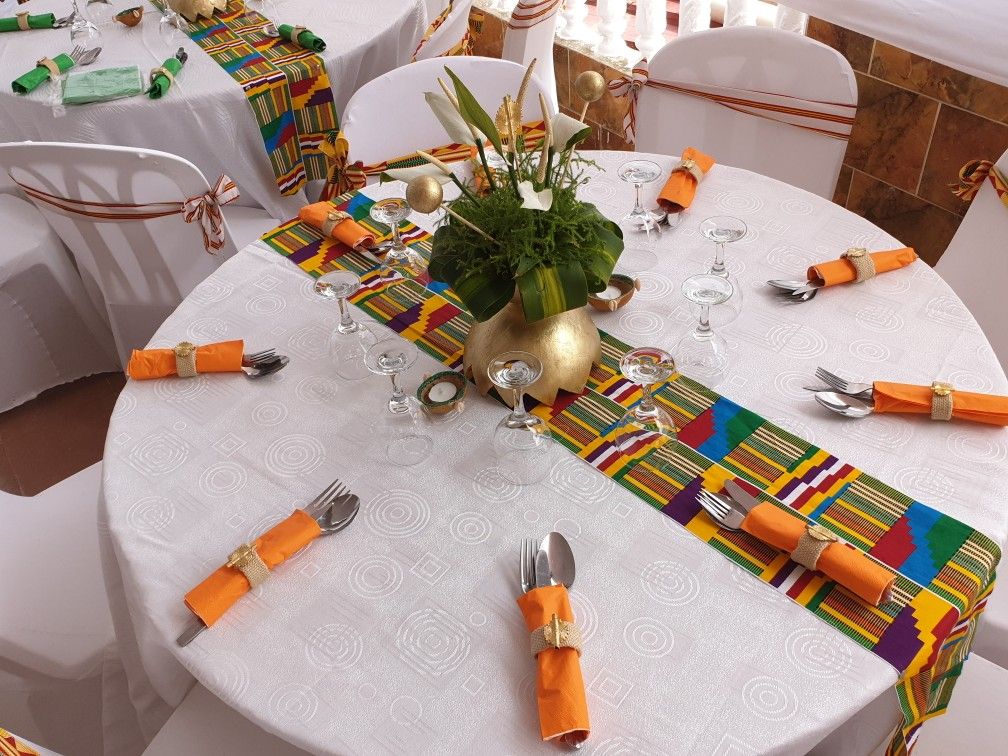Table ronde dressée avec un chemin de table en tissu kente, des serviettes orange et un centre de table doré
