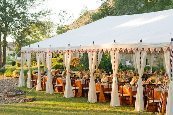 Tente blanche ouverte sur une pelouse, rideaux blancs et tables dressées de fleurs